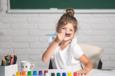 Boyama kalemleriyle resim çizen çocuk. Okulda sanat ve zanaat dersinin tadını çıkarırken mutlu bir şekilde gülümseyen küçük kızın portresi. Çocukların yaratıcı eğitim konsepti