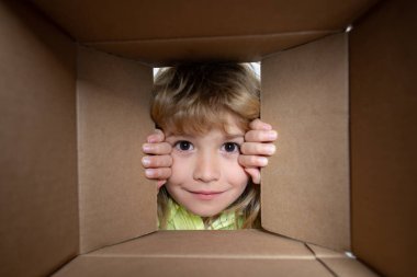 Child open paper cardboard box. Kid boy unpacking and opening carton box looking inside with surprise face. Parcels and delivery.