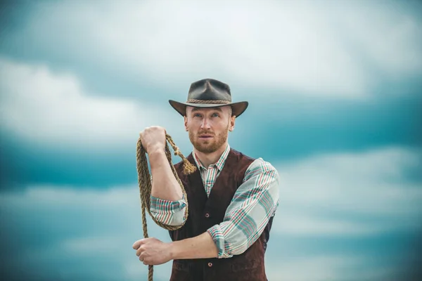 Homem ocidental sexy com chapéu de cowboy. Cowboy com corda de laço no fundo do céu. — Fotografia de Stock