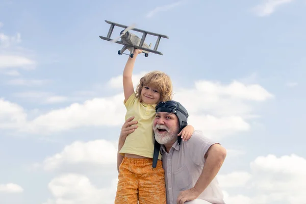 Jeune petit-fils et vieux grand-père jouant avec l'avion ensemble sur ciel bleu. Enfant mignon avec grand-père jouant en plein air. Week-end avec grand-père. — Photo