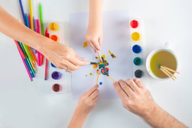 Hands of a family drawing with pencil and paints. Top view to white table with art supplies. Kids learning painting.