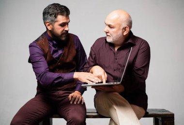 Yaşlı baba ve yetişkin oğul internetten alışveriş yapmak, internette gezinmek veya iş görüşmesi yapmak için dizüstü bilgisayar kullanıyorlar..