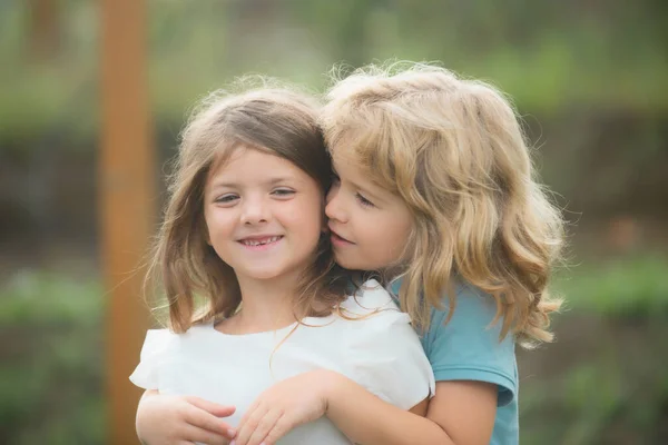 Adorable happy kids outdoors on summer day, little boy kissing a girl. Lovely little boy and girl, have fun and hugging outdoor. Funny kids face. — Stock Photo, Image