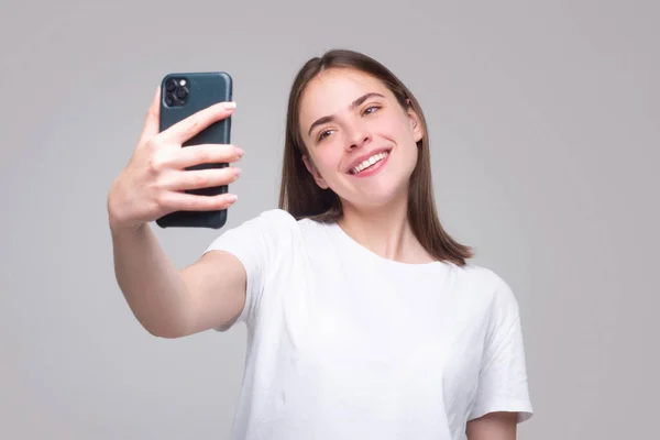 Happy young african woman casually dressed standing isolated over gray background, holding mobile phone. Girl making taking selfie. — Fotografia de Stock