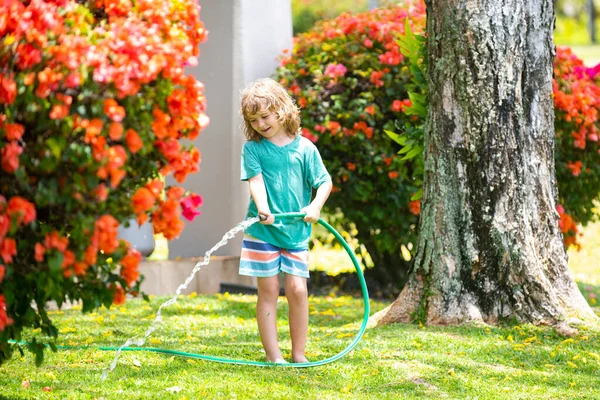 Kids play with water garden hose in yard. Outdoor children summer fun. Little boy playing with water hose in backyard. Party game for children. Healthy activity for hot sunny day.