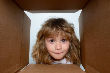 Çocuk paketleri açıyor ve karton kutuyu açıyor. Sürpriz bir suratla içeri bakıyor. Çocuklar şaşırmış yüz ifadeleri.