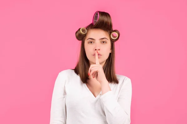 Segredos femininos. Uma mulher com rolos a mostrar sinais secretos. Uma dona de casa engraçada. Retrato de close-up da jovem está mostrando um sinal de silêncio com shhh. — Fotografia de Stock