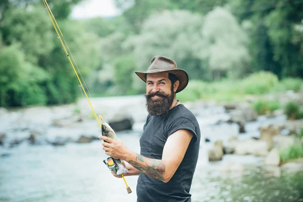 Fischer auf Fluss oder See mit Angelrute. Hipster-Bärtiger beim Forellenfang. — Stockfoto