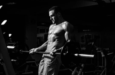 Spor adamı halter kaldırarak biceps yapıyor. Çıplak gövdeli genç kaslı adam spor salonunda çalışıyor. Spor yapan atletik erkek sporcu. Spor konsepti.