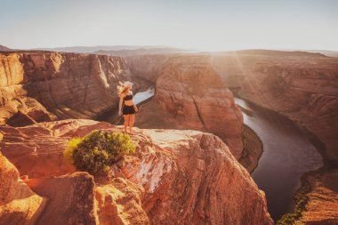 Horseshoe Bend ve Colorado Nehri 'ne bakan genç bir kadın. Ünlü yürüyüş yeri. Glen Canyon, Arizona, ABD. Seyahat ve macera konsepti. Amerikalı turist.