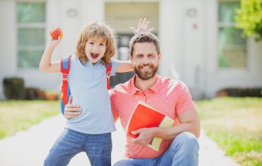 Öğretmenler günü. Amerikan baba ve oğlu okul parkında yürüyor. Okul bahçesinde mutlu bir aile.