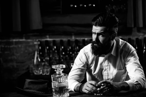 Charmant homme tient un verre de whisky et regarde loin tout en étant assis dans le bar à l'intérieur. — Photo