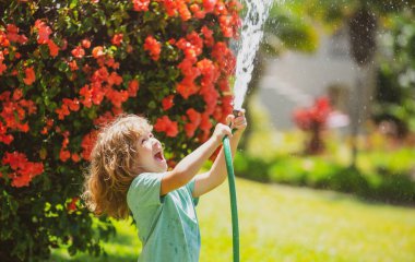 Çocuk eğleniyor. Komik çocuk doğal ortamda mutlu bir şekilde gülümsüyor. Küçük çocuk temiz havada eğleniyor. Komik olmak en büyük özelliklerimden biridir. Güneşli yaz gününde bahçedeki çiçekleri sulamak..