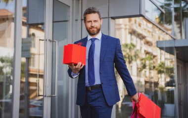 Harika bir hediye. Elinde hediye kutusu olan ve şehrin karşısında dururken gülümseyen adam.