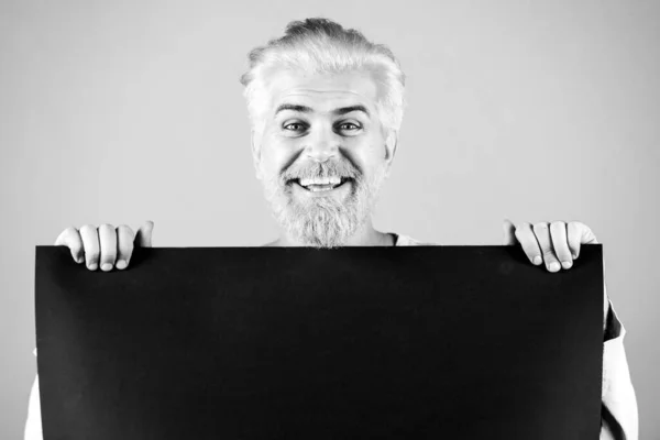 Happy Man met een leeg vel zwart papier. Kleurrijk atelierportret op geïsoleerde achtergrond. Reclamebord voor kantoorpersoneel. — Stockfoto