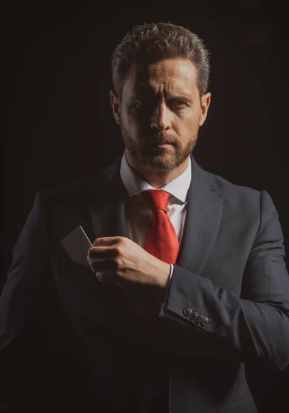 Retrato de un elegante hombre de negocios apuesto aislado en negro. Guapo hombre de negocios de mediana edad con tarjeta de crédito en traje posando sobre un fondo negro con espacio para copiar. — Foto de Stock