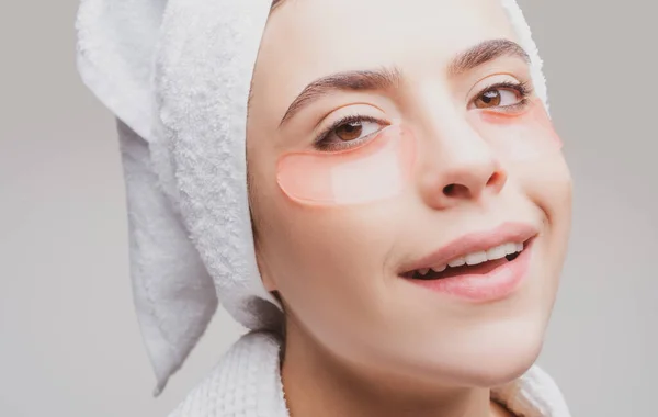 Close up portrait girl with towel on head. Portrait of beauty woman with eye patches showing an effect of perfect skin. Brunette spa girl. Eyes mask cosmetic patches woman face closeup. — Stock Photo, Image