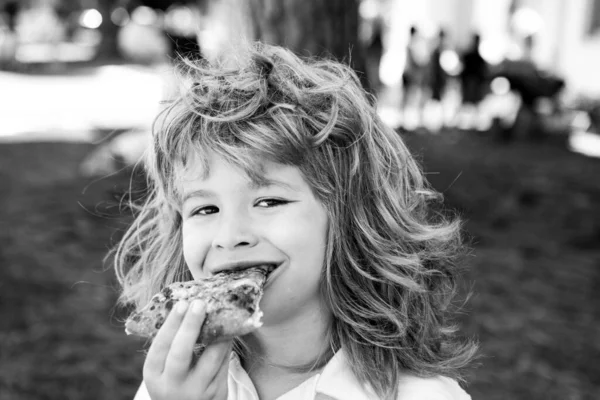 Un ragazzo con un morso di pizza. Il bambino mangia la fetta di pizza al salame piccante. Faccia divertente per bambini. — Foto Stock