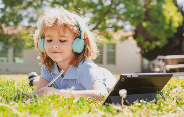 Liten skolpojke elev använda anteckningsbok eller surfplatta och skriva nomework i skolparken. Hälsosamt skolbarn. — Stockfoto