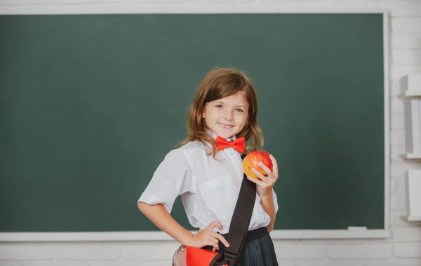 Gelukkig glimlachend tiener meisje, kind schoolmeisje met draagt schhol uniform houden rugzak op schoolbord achtergrond op zoek naar camera. Begrip onderwijs, leren en kinderen. — Stockfoto