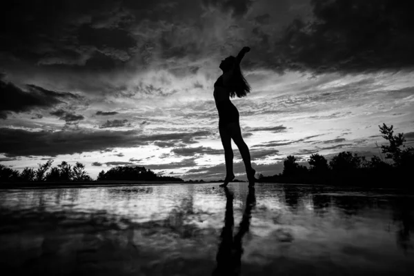 Чорний силует красивої дівчини або красивої жінки, сексуальна струнка модель, з довгим волоссям на морському пляжі на заході сонця на фіолетовому фоні неба — стокове фото