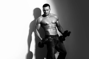 Dambılı yakışıklı kaslı adam. Seksi üstsüz genç erkek fitness modeli. Göğüs kaldıran güçlü genç bir adamın çıplak gövdesi gri arka planda dambıl egzersizi yapıyor..