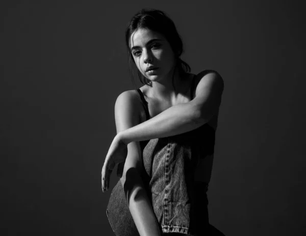Portret stylowej dziewczyny w czarnym staniku i dżinsach jeansowych siedzącej i patrzącej w kamerę. — Zdjęcie stockowe
