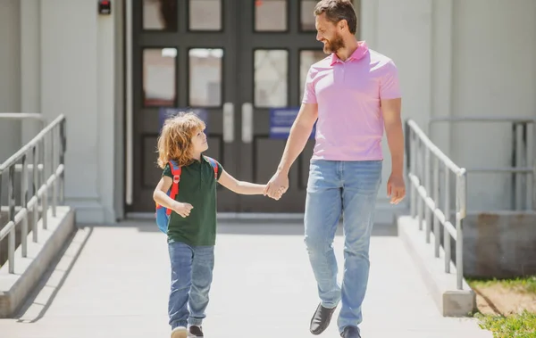 Father supports and motivates son. Parent taking child to school. Pupil of primary school go study with backpack outdoors. Parent with child in front of School gates. — Stock Photo, Image