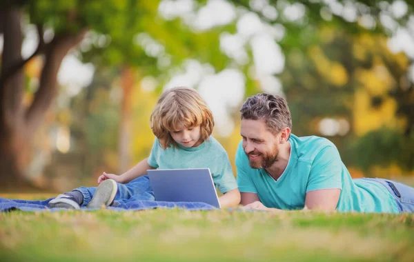 Ευτυχισμένος πατέρας με γιο που χρησιμοποιεί λάπτοπ στο πάρκο. Παιδί με σημειωματάριο έξω το καλοκαίρι. Παιδί σε πάρκο εξ αποστάσεως εκπαίδευσης. — Φωτογραφία Αρχείου