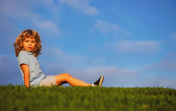 Niño pequeño con una cara de expresión linda sentado en la hierba. Alegre niño divirtiéndose en verde prado de verano. —  Fotos de Stock