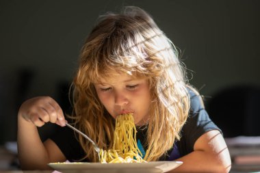 Masada oturan genç bir çocuk yüzünde komik bir ifadeyle sağlıklı yiyecekler yiyor. Evde makarna yiyen şirin bir çocuk..