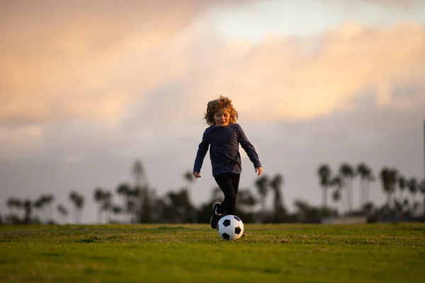 Boy kicking football ball. Soccer child play football. Training for sport children in park. Concept of children sport. Excited child boy kicking ball in the grass outdoors. — Zdjęcie stockowe