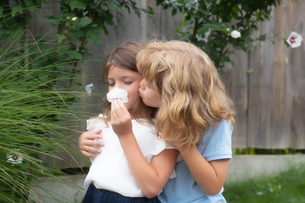 Knuffelen en zoenen kinderen paar. Kleine lieve kinderen buiten. Kinderen in het zomerpark, dicht bij elkaar. Kinderen houden van elkaar. Romantisch, jongen en meisje geven een bloem voor liefde en romantiek. — Stockfoto