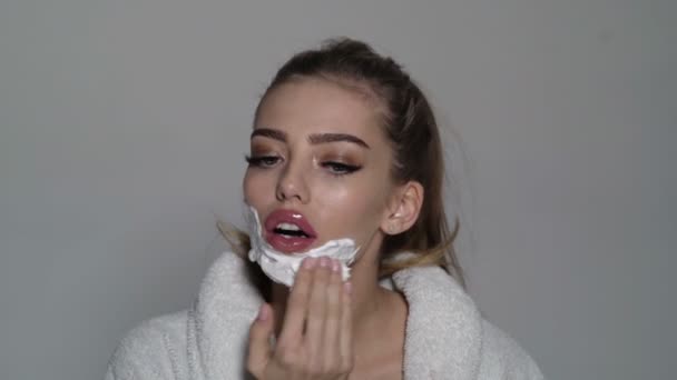 Beautiful young caucasian woman shaving her face by razor. Pretty girl with shaving foam on her face. — ストック動画