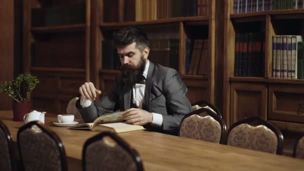 Hombre barbudo en traje clásico leer libro en la biblioteca. Humor clásico inglés. Literatura clásica. Hombre leyendo libro, beber té en la estantería. Estudiante adulto seguro en la biblioteca. — Vídeos de Stock