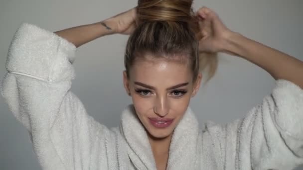 Girl in a bathrobe pulls her hair into a tail. Close up portrait of sexy sensual woman. — Stock video