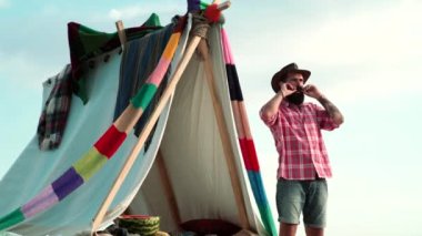 Çadırın yanında kamp yapan genç adam, mutlu erkek macera yolculuğunun tadını çıkarıyor..