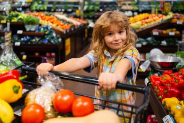 Süpermarkette meyve alan bir çocuk. Çocuk bakkal alışverişi. Alışveriş arabalı çocuk marketten taze sebze seçiyor. Sağlıklı çocuk yemekleri. Süpermarketteki çocuk sebze alır.