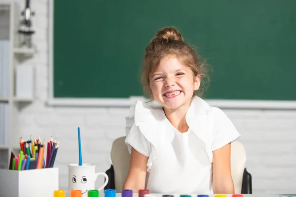 Leuke kleine kleuter kind meisje tekening op school. Kindermeisje schilderen op de basisschool. Grappig schoolmeisje gezicht. — Stockfoto