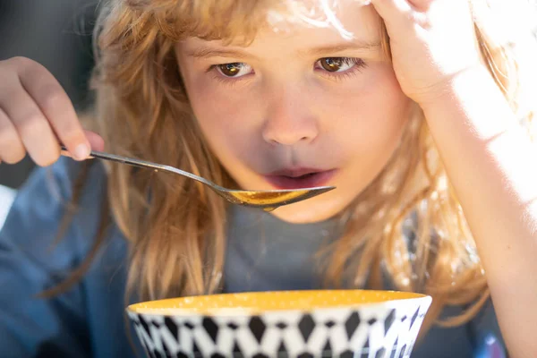 Happy child boy with spoon eats itself soup. Kid eating food on kitchen. — Stockfoto