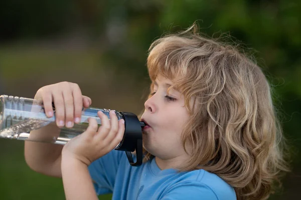 Kid drinking water outdoor. Close up portrait of boy drink water from bottle in the garden. — Foto Stock