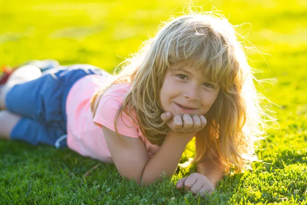 Mutlu küçük çocuk bahar günü çimlerin üzerinde yatıyor. Parktaki yeşil çimlerin üzerinde yatan gülümseyen bir çocuğun portresi. Bahçedeki çayırda küçük şirin bir çocuk..