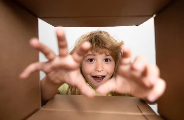 Kid unpacking and opening carton box, and looking inside with surprise face. Child take by hand gift fron open box. — Stock Photo, Image