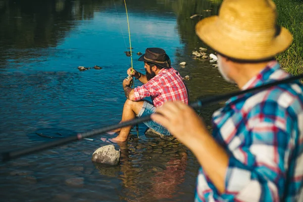 Nehirde balık tutan iki erkek arkadaş. Yaşlı baba ve oğlu nehir kenarında olta balıkçılığı yapıyor. Eğlence etkinliği. — Stok fotoğraf
