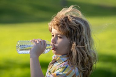 Parktaki evcil hayvan şişesinden su içen çocuk. Çocuk içiyor. Parkta su içen, elinde plastik şişe tutan bir çocuk. Susamış çocuk.
