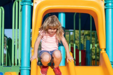 Kaydırağın üzerinde oynayan mutlu çocuk. Çocuk parkında oynarken sevimli küçük çocuk komikliği. Yaz çocukları.