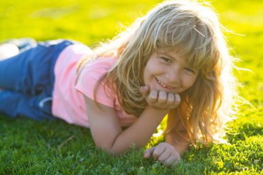 Yaz çocuğu suratı. Çimen geçmişi olan gülümseyen çocuk. Mutlu bir çocukluk. Çimenlerde yatan çocuk. Sahada yazın tadını çıkaran tatlı bir çocuk. Rüya gören çocuklar konsepti.