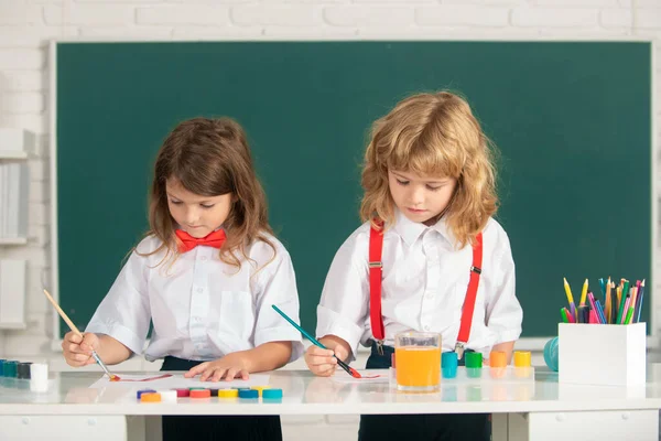 Roliga elever ritar i klassrummet på skolans svarta tavlan bakgrund. Skolkamrater barn måla tillsammans i klassen. — Stockfoto