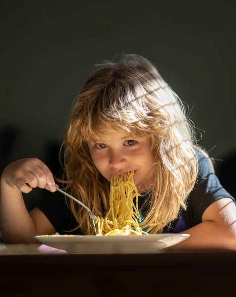 Happy child boy with spoon eats itself. Cute little kid eating spaghetti pasta at home. — Stok fotoğraf