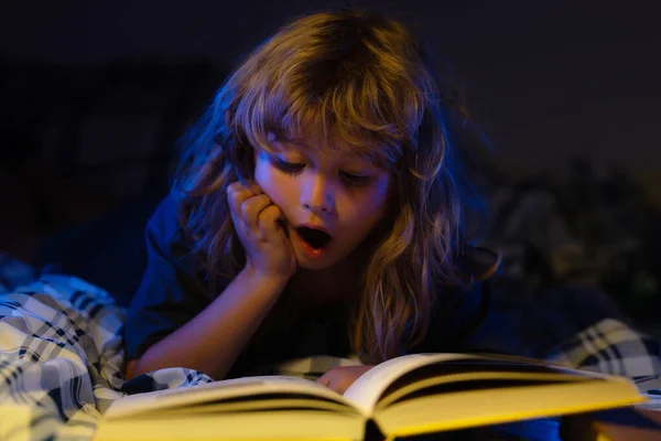 Happy childhood, dreaming child. Cute excited boy reading book. Child with open book. Homeschool lesson. Concentrated little boy on bed reading book at home. — стоковое фото